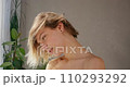 Attractive young woman blow drying hair, while looking out window in bathroom. Side view of caucasian female with bare shoulders drying and touching short dyed hair in morning. Daily routine concept. 110293292
