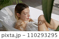 Relaxed blonde lady pouring body wash on sponge, while lying in bathtub. Above view of stunning, calm female scrubbing with sponge, while taking bubble bath in hotel. Self care, cosmetic, spa concept. 110293295