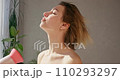 Stunning young female blow drying hair and looking out window in bathroom. Side view of blonde woman with bare shoulders touching short airy hair, while drying in sunny morning. Concept of lifestyle. 110293297