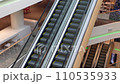 Escalator in a large multi-storey shopping center. High angle view. Going up and down an escalator with glass walls and metal steps in a sparsely populated business center 110535933