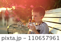 Boy sits on a bench and eats ice cream wrapped in a waffle with chocolate and strawberries 110657961