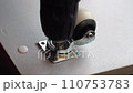 The screwdriver tightens the screw. An electric handheld screwdriver drives a black hardened screw into a wooden slab and secures a furniture wheel. Furniture assembly workshop. Close-up of screw 110753783