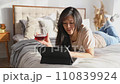 Happy beautiful woman in casual clothes talking on video call on digital tablet lying on the bed. Playing game shopping online relaxing. 110839924