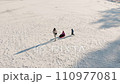 Young adult mother wear warm jacket enjoy have fun sledging two cute little sibling kids boy girl at frozen white snow lake field against clean blue sky landscape bright sunny cold winter day. Outdoor 110977081