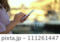 Woman with phones in her hands in the rays of the setting sun against the background of a boat station. 111261447