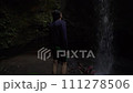 A young man stands alone at the waterfall and admires its view, looking up from the bottom of the river canyon. Rear view 111278506
