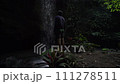 A young man stands alone at the waterfall and admires its view, looking up from the bottom of the river canyon. Rear view 111278511