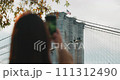 Female tourist taking pictures of the Brooklyn Bridge with an American Flag waving in the wind 111312490