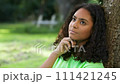 Beautiful mixed race African American girl biracial teenager young woman outside thoughtful, sad or depressed sitting leaning against a tree 111421245