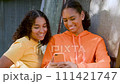 Two beautiful, happy, smiling mixed race African American girls teenagers young women outdoors in the city using a smartphone or cell phone for social media or text messaging 111421747
