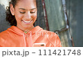 Beautiful mixed race African American girl teenager young woman in a city wearing an orange hoodie using her smart cell phone for social media 111421748