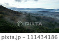 Foggy sky blankets natural landscape of mountain range, trees, and grassland. 111434186