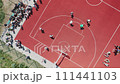 Aerial top down view of teenagers playing basketball on the outdoor summer basketball court. Teenagers are trying to throw the ball into the basketball basket on the outdoor sports ground. 111441103