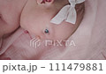 Portrait of a beautiful newborn baby girl lying in a white cot under a pink plaid with ruffles at home with a bow on her head and looking around. 111479881