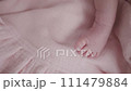 Portrait of a beautiful newborn baby girl lying in a white cot under a pink plaid with ruffles at home with a bow on her head and looking around. 111479884