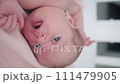Portrait of a beautiful newborn baby girl lying in a white cot under a pink plaid with ruffles at home with a bow on her head and looking around. Vertical 111479905