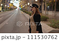 American side shot in motion of a pretty woman in a black coat and light brown dress crossing a street 111530762