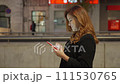 Medium lateral moving shot of a pretty woman with the smartphone and black coat and light brown dress 111530765