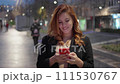 Medium frontal shot of a pretty woman with the smartphone and black coat and light brown dress 111530767