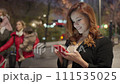 Medium lateral shot of a pretty woman with the smartphone and black coat and light brown dress 111535025