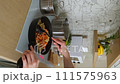 Hands of woman mixing fried salmon pieces with mushrooms and vegetables into a frying pan with pasta 111575963