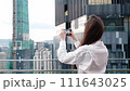 A woman shooting video on her phone on the roof of a building against the backdrop of a big city skyscrapers and business center, a business trip for work. 111643025