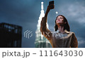 Woman captures video on her phone at night with a smile against a backdrop of glowing skyscrapers, nightlife and freelance tourist 111643030