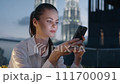 A woman looks at her phone, smiles and types a message against a backdrop of a night city and glowing buildings, work and leisure. 111700091