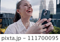 Business woman with phone in hand fun laughing and smiling in the background of the city and skyscrapers in the afternoon, lifestyle modern urban freelancer 111700095
