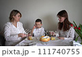 a family of three, mother, teenage daughter and little son, eating cake in pajamas at a table with tulips 111740755