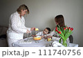 a family of three, mother, teenage daughter and little son, eating cake in pajamas at a table with tulips 111740756