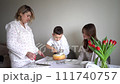 a family of three, mother, teenage daughter and little son, eating cake in pajamas at a table with tulips 111740757