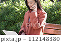一位女士在公園的長椅上使用電腦打電話 112148380
