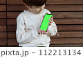 a toddler sits on a bench and looks on the phone with green screen 112213134