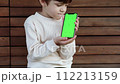 a toddler sits on a bench and looks on the phone with green screen 112213159