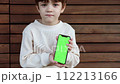 a toddler sits on a bench and looks on the phone with green screen 112213166