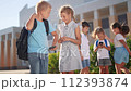 children group school children look at the smartphone video. school learning kid concept. lifestyle group of kids with backpacks playing smartphone near the school building outdoors 112393874