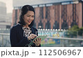 Smiling Elderly Woman Using Tablet, Texting with Friends while Standing Outside in Formal Black Suit. Senior Manager Working Outdoors, Distantly Chatting with Colleagues. People and Technology Concept 112506967