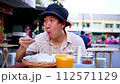 Young adult Asian man enjoys eating a local Thai food in the street food stall shop in Bangkok, Thailand. Solo backpacker eating street food on table in the street. Southeast Asia tourism concept 112571129