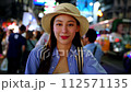 Young adult Asian woman smiles in front of camera on the street at night in Bangkok, Thailand. Solo backpacker enjoying travel vibes on street. Southeast Asia tourism concept 112571135