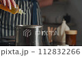A woman in a striped apron makes wax scented candles. She adds aromatic oil to the wax.Close up. 112832266