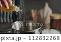 A woman in a striped apron makes wax scented candles. She adds aromatic oil to the wax.Close up. 112832268