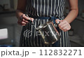 The process of making wax scented candles. A woman in a striped apron checks the temperature of melted wax with a thermometer. 112832271