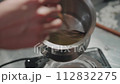 A woman in a striped apron makes wax candles. She stirs the melted wax in a pan. The creative process of making wax scented candles. 112832275