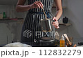 A woman in a striped apron makes wax candles. She stirs the melted wax in a pan.The creative process of making wax scented candles. 112832279