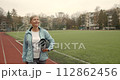 Mature adult woman practicing fitness outdoors holding yoga mat. Sports for elderly people. 112862456