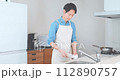 A man wearing an apron washing dishes in the kitchen 112890757