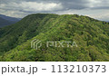 Aerial view flying along a mountain ridge covered in thick, lush forest and lake 113210373