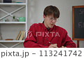 A young male student wearing glasses gives a presentation of his work, sitting at a table indoors at home. The guy opened a clipboard with graphs and looking at the camera, shows them. 113241742