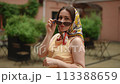 Slow motion. A woman in a headscarf turns to the camera and lowers her sunglasses, looking at the camera smiling. A woman puts on sunglasses while standing outdoors on a summer day. 113388659